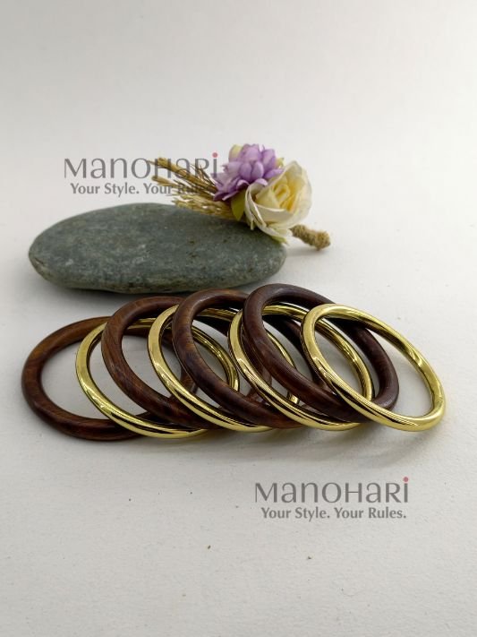 MN-BG-WOD-VRW-01_1 **The Vanya Rustic Wood Bangles Set showcases the timeless beauty of handcrafted wooden jewellery with a warm rustic brown finish accented by elegant gold-tone detailing. This set of **8 lightweight wooden bangles** is thoughtfully designed to offer both comfort and style, featuring an **inner diameter of approximately 6 cm** for a comfortable fit. Perfect for stacking or wearing individually, these versatile bangles effortlessly complement **Kerala Kasavu sarees, cotton sarees, silk sarees, kurtis, dresses, and Indo-western outfits**. Ideal for **Onam, weddings, festivals, office wear, casual outings, cultural celebrations, and everyday styling**, the **Vanya Rustic Wood Bangles Set** adds a touch of natural elegance to every look. Exclusively curated by **Manohari Style**, this beautifully crafted bangle set blends rustic charm, modern versatility, and timeless craftsmanship, making it a must-have accessory for every woman's jewellery collection.**