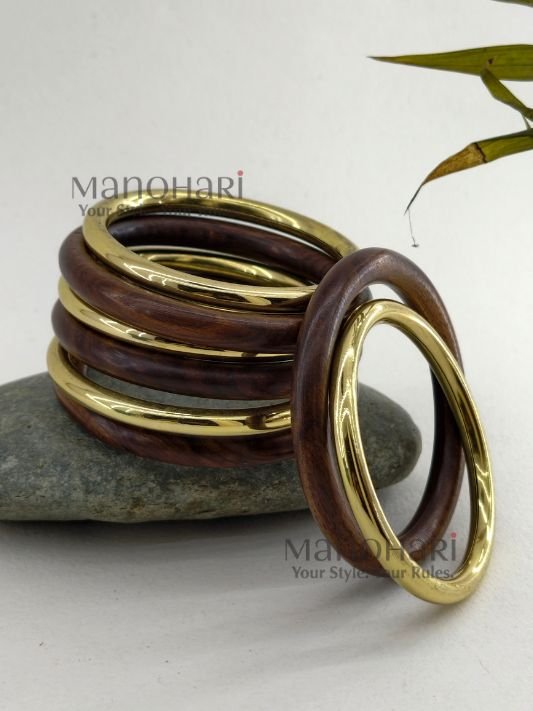 MN-BG-WOD-VRW-01_2 **The Vanya Rustic Wood Bangles Set showcases the timeless beauty of handcrafted wooden jewellery with a warm rustic brown finish accented by elegant gold-tone detailing. This set of **8 lightweight wooden bangles** is thoughtfully designed to offer both comfort and style, featuring an **inner diameter of approximately 6 cm** for a comfortable fit. Perfect for stacking or wearing individually, these versatile bangles effortlessly complement **Kerala Kasavu sarees, cotton sarees, silk sarees, kurtis, dresses, and Indo-western outfits**. Ideal for **Onam, weddings, festivals, office wear, casual outings, cultural celebrations, and everyday styling**, the **Vanya Rustic Wood Bangles Set** adds a touch of natural elegance to every look. Exclusively curated by **Manohari Style**, this beautifully crafted bangle set blends rustic charm, modern versatility, and timeless craftsmanship, making it a must-have accessory for every woman's jewellery collection.**