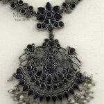 **Varnika Floral Pearl Heritage Necklace crafted from premium brass with a silver replica finish, featuring an intricate floral pendant adorned with elegant black stones, measuring 6 × 5 cm on a 21 cm statement necklace for timeless ethnic elegance.**