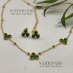 **Juwana Floral Heritage Necklace Set crafted from premium gold-plated metal, featuring radiant emerald green floral daisy motifs, a delicate gold link chain, and matching floral earrings for women.**