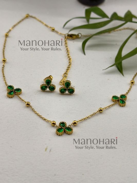 **Juwana Floral Heritage Necklace Set crafted from premium gold-plated metal, featuring radiant emerald green floral daisy motifs, a delicate gold link chain, and matching floral earrings for women.**