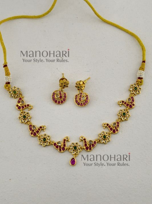 **Morika Peacock Heritage Necklace crafted from a premium alloy metal base with a luxurious gold-plated antique finish, adorned with vibrant Kemp-inspired stones, AD/CZ accents, Kundan-style detailing, pearls, and decorative beads, featuring an elegant peacock motif with matching earrings for timeless bridal and festive elegance.**